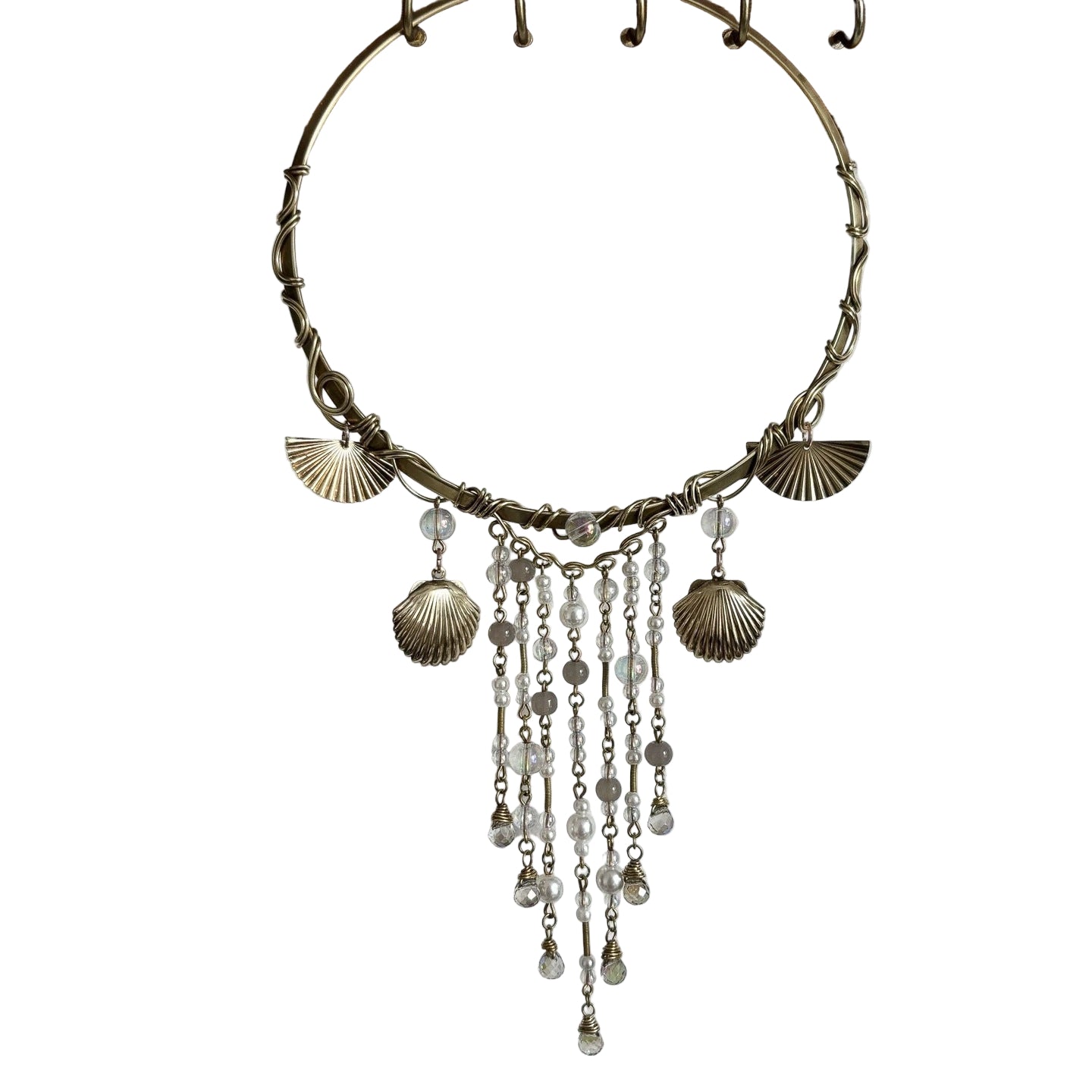 Bronze necklace with shell and bead charms hanging on a wooden stand against a white background