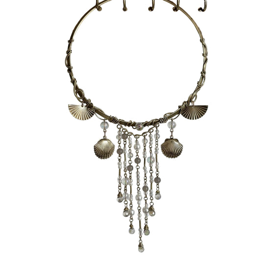 Bronze necklace with shell and bead charms hanging on a wooden stand against a white background